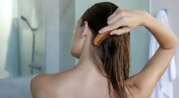 Une femme se peigne les cheveux mouillés, préoccupée par la **chute de cheveux** causée par l'**eau calcaire**.