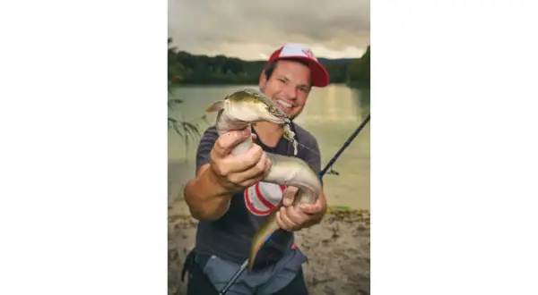 Glücklicher Angler hält einen Aal, der an einer Fischfetzen-Montage hängt.