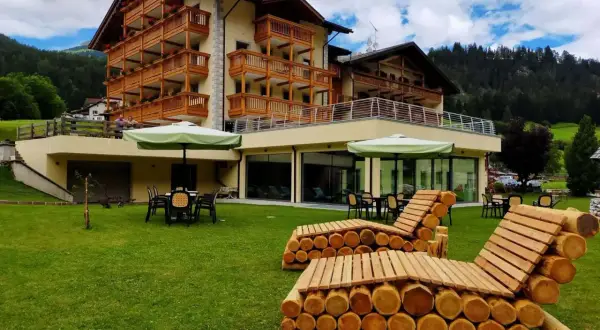 Hotel Dolomia Soraga: un'oasi di relax con vista sulle montagne. Panchine in legno e prato verde invitano al riposo.