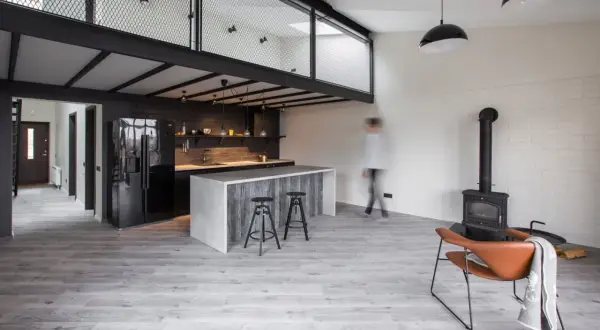 Nowoczesna kuchnia z wyspą i antresolą. Inspiracje dla loftowych wnętrz, gdzie industrialny styl łączy się z przytulnością kominka i wygodnym fotelem.