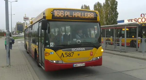 Żółty autobus linii 166 w Warszawie, z napisem "166 PL. HALLERA" na wyświetlaczu, stoi na przystanku obok centrum handlowego Tesco.