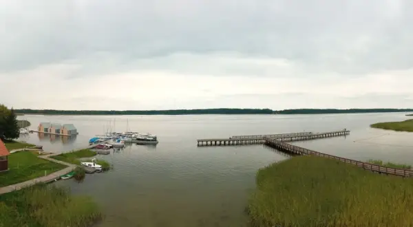 Widok na jezioro, gdzie wypływa roś. Widać pomosty, łodzie, pływające domki i plażę.