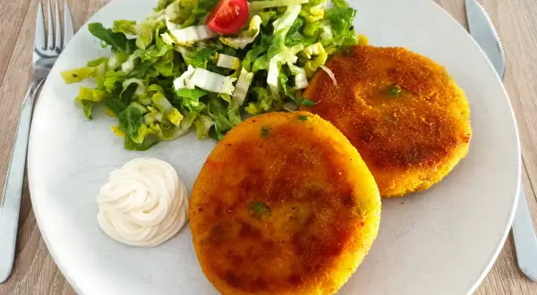 Zwei goldbraune, vegetarische Frikadellen mit einem frischen Salat und Mayonnaise auf einem Teller.