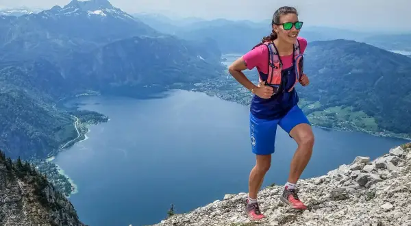 Läuferin im Gebirge, die zeigt, wie verbessere ich meine ausdauer durch anspruchsvolles Gelände. Bergsee und Gipfel im Hintergrund.