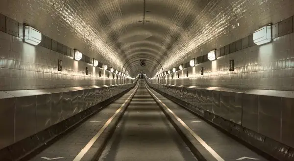 Der lange, beleuchtete Gang des alten Elbtunnels mit seinen gekachelten Wänden und Lichtern, die eine Perspektive erzeugen.