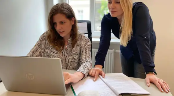 Dwie kobiety pracują nad dokumentami i laptopem, przygotowując wniosek o rozwód online.