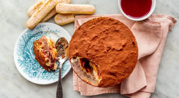 Délicieuse zuppa inglese recette, avec une part déjà servie sur une assiette ornée. Des biscuits à la cuillère et une coupelle de coulis complètent ce dessert gourmand.