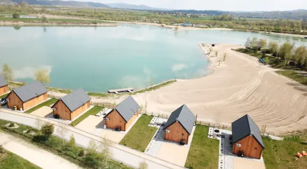 Drewniane domki nad turkusową wodą, idealne na wypoczynek w stylu kąpielisko Mała Chorwacja. Piękny piasek i zieleń wokół.