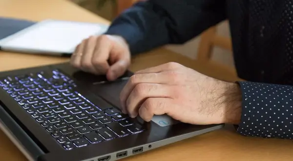 Dłonie pracują na laptopie z podświetlaną klawiaturą. Procesor AMD Ryzen 5 5600H zapewnia płynność pracy.