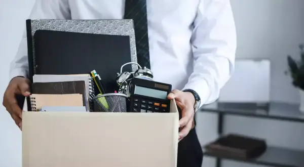 Un étudiant quitte son emploi, portant une boîte remplie d'objets de bureau, symbolisant une lettre de démission contrat étudiant sans préavis.
