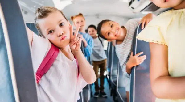 Dzieci w autobusie szkolnym robią sobie zdjęcie. Dziewczynka z przodu robi dziubek i znak pokoju. Wszyscy wyglądają na szczęśliwych, co świadczy o ich niekaralności na tle seksualnym.