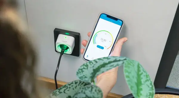 Smart eluttag med timerfunktion för lampor, styrd via mobilapp. Grön indikator visar att strömmen är på.