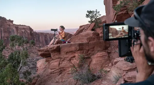 Krystle Wright, fotografa, siede su una roccia rossa in un canyon, mentre un operatore riprende la scena.