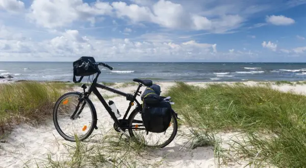 Rower z sakwami na plaży, gotowy do podróży trasą rowerową R10. Morze i niebo w tle.