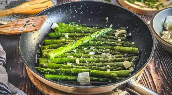Grüner Spargel wird in einer Pfanne mit Käse und Kräutern zubereitet. Ein köstliches Gericht, das zu vielen Spargel Rezepten passt.