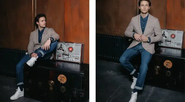 Junger Mann im lässigen Look: Sakko Herren sportlich zu Jeans, dazu weiße Sneaker. Ein Vintage-Tonbandgerät steht daneben.