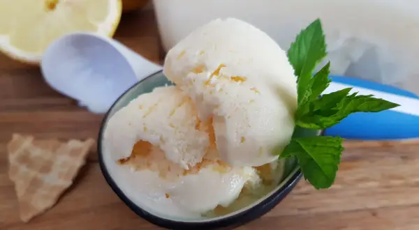Erfrischendes zitroneneis mit joghurt, garniert mit Minze, daneben eine Waffel und Zitronenspalten.