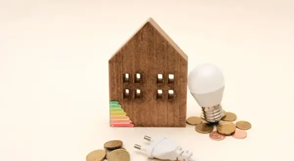 Drewniany domek z etykietą energetyczną, żarówką i monetami. Zastanawiasz się, ile prądu zużywa lampka nocna?