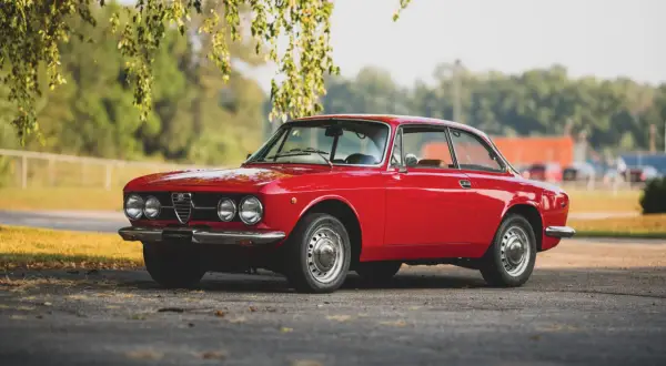 Klasyczny czerwony Alfa Romeo GT 1300 Junior, jeden z pięknych alfa romeo modele, stoi pod drzewem.