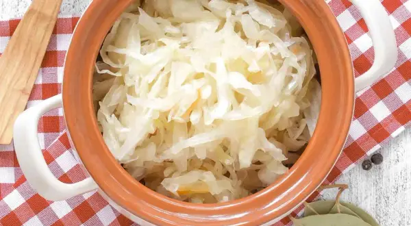 Sauerkraut in einem Tontopf mit kariertem Tuch, Lorbeerblättern und Pfefferkörnern.