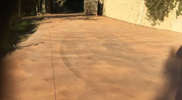 Un camino de **suelo hormigon pintado** de color terracota, con marcas de neumáticos, conduce a una puerta abierta.