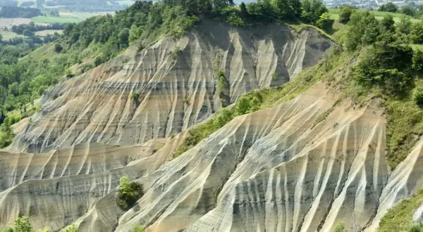 Le ravin de Corboeuf, un paysage spectaculaire aux strates colorées sculptées par l'érosion, dominé par une forêt verdoyante.