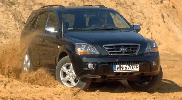 Czarny Kia Sorento 1. pokonuje piaszczysty teren, wzbijając tumany kurzu.