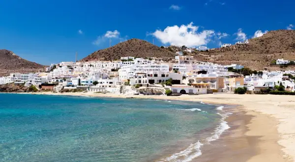 Costa blanca con aguas verde esmeralda, roquetas de mar, y casas blancas en la ladera.