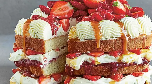 En generös tårta med lager av sockerkaka, vispgrädde, färska jordgubbar och en härlig jordgubbsmousse tårtfyllning, toppad med mer grädde och karamellsås.