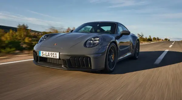 Szary Porsche 911 GTS sunie po krętej drodze, otoczony jesiennym krajobrazem.