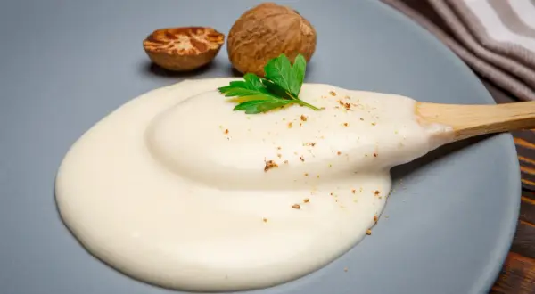 Krämig bechamelsås på en tallrik med muskotnötter och persilja. Perfekt för ditt bechamelsås recept.