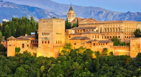 Alhambra, jeden z najpiękniejszych zabytków w hiszpańskich miastach, wznosi się na wzgórzu otoczony zielenią, z górami w tle.