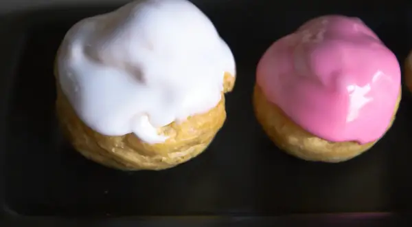 Deux petits choux garnis, l'un d'un glacage sucre glace blanc, l'autre d'un glacage rose.