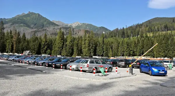 Parking Morskie Oko, cena za postój. Rząd samochodów na kamienistym parkingu, w tle las i góry.