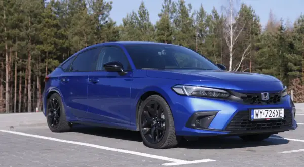 Błękitny Honda Civic 11. generacji z czarnymi felgami zaparkowany na tle lasu.