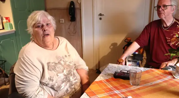 En kvinna med vitt hår sitter vid ett bord. Hon ser trött ut, som om hon inte orkar med sin dementa mamma. En man sitter mittemot.