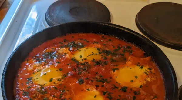 En varm och bubblande shakshuka med ägg i tomatsås, perfekt för ett mysigt frukostrecept.