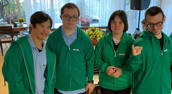 Quattro ragazzi con sindrome di Down, vestiti con felpe verdi, sorridono e posano per una foto.