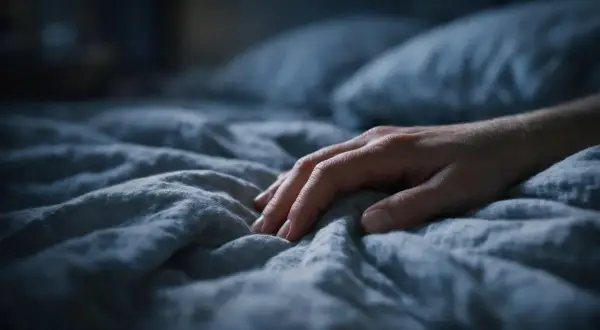 Mano su lenzuola stropicciate, un senso di ansia a mille nella notte.