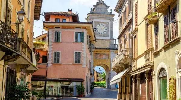 Un vicolo nel salò centro storico, con palazzi color pastello e un arco con orologio che conduce verso il lago.