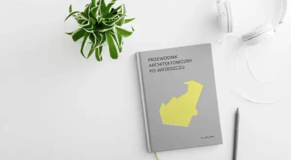 Przewodnik architektoniczny po Wrzeszczu, słuchawki i długopis na białym tle. Zielona roślina w doniczce.