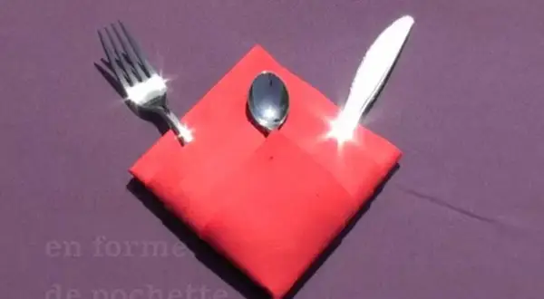 Pliage serviette Noël porte couvert en forme de pochette rouge, avec une fourchette, une cuillère et un couteau.
