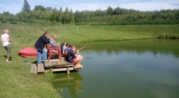 Dzieci i dorośli łowią ryby na drewnianym pomoście. Malownicze łowisko pod lasem Bielany Wrocławskie.