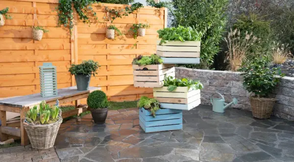 Fioriere in legno fai da te impilate, piene di verdure fresche, creano un angolo verde su un patio in pietra.