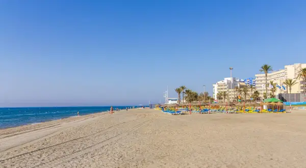 Amplia playa de la urbanización de Roquetas con sombrillas, tumbonas y edificios hoteleros al fondo.