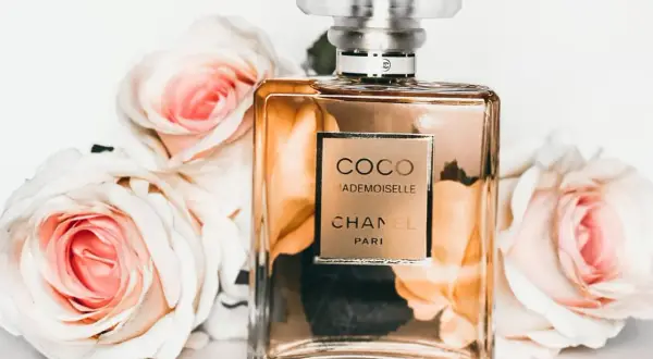 Szklana butelka perfum Chanel Coco Mademoiselle otoczona jasnoróżowymi różami.