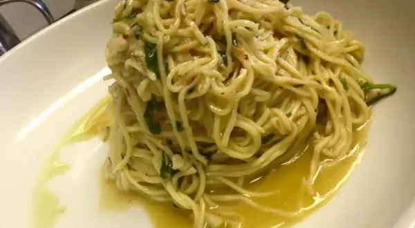 Un piatto di spaghetti aglio olio e peperoncino cremosi, conditi con prezzemolo fresco e un filo d'olio d'oliva.