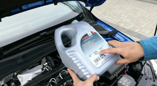 Osoba trzymająca kanister oleju silnikowego TITAN GT1 PRO C-3 SAE 5W-30 nad silnikiem. Czy można mieszać oleje silnikowe? Sprawdź specyfikację!