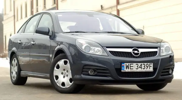 Ciemnoszary Opel Vectra C z polskimi tablicami WE 3439F. Widać jego przednie reflektory, atrapę chłodnicy z logo Opla i zderzak.