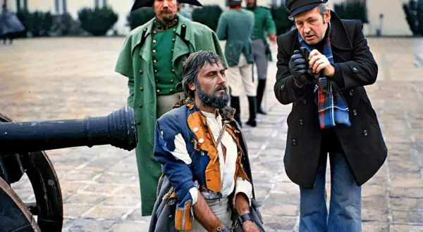 Scena z planu filmowego w polska lat 80. Uwięziony mężczyzna w zniszczonym stroju, obok żołnierze i reżyser.